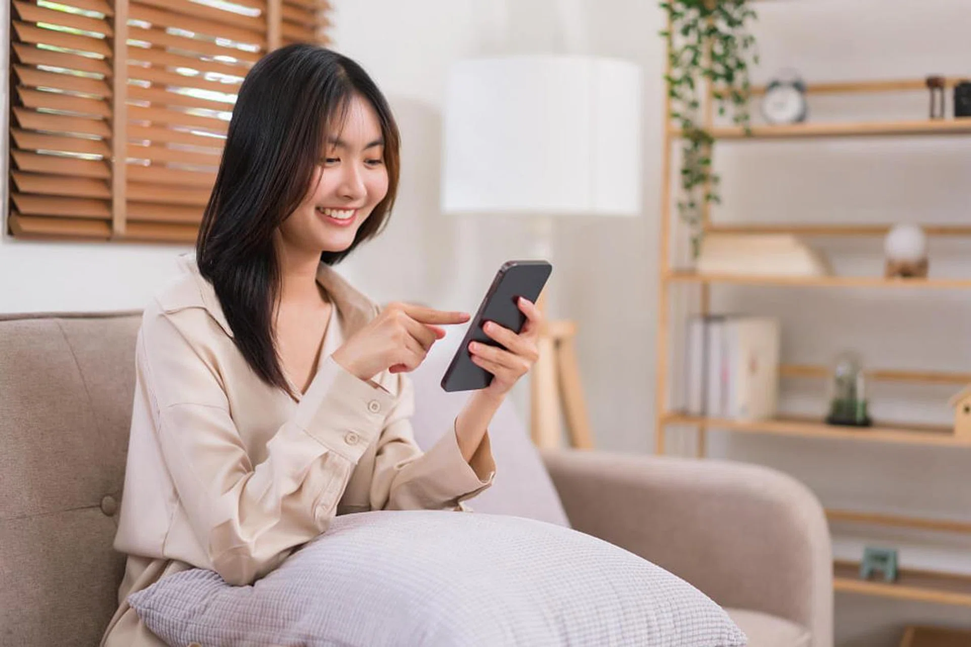 asian lady using smartphone scrolling through social media content at home
