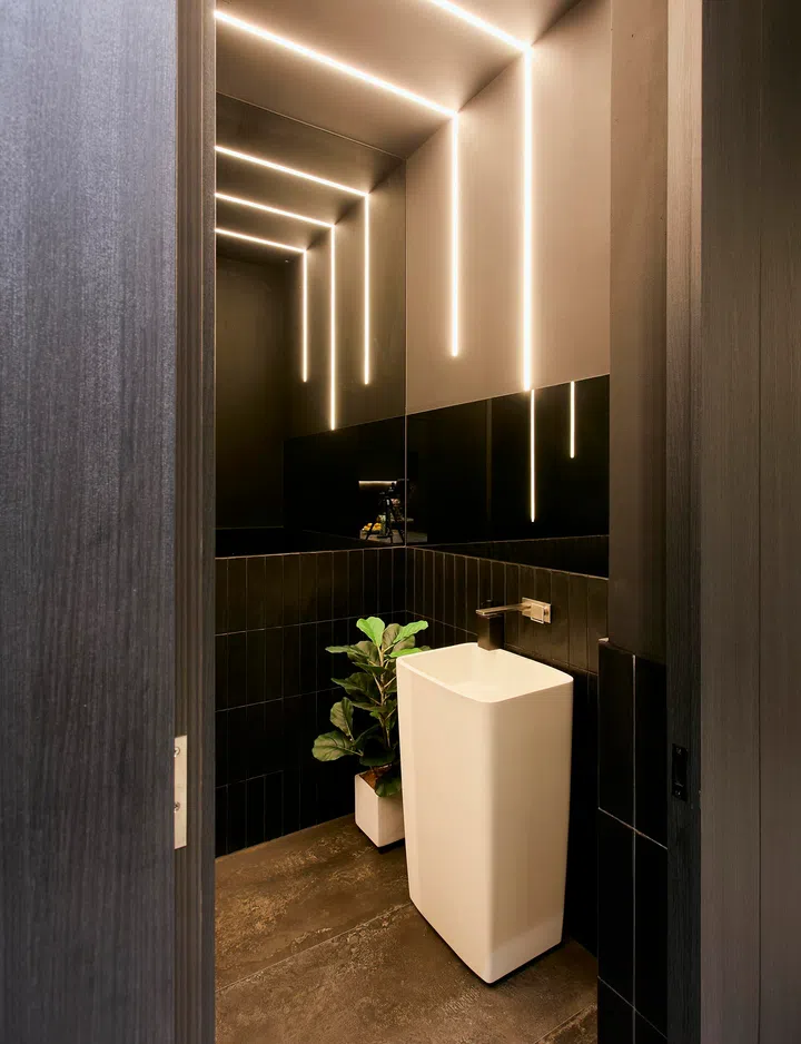 The compact powder room features dark finishing and vertical lighting for a more intimate, contrasting atmosphere.