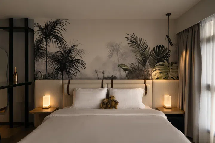The king-sized bed anchors the room, set against a soft tropical mural that evokes the calm of a resort suite.