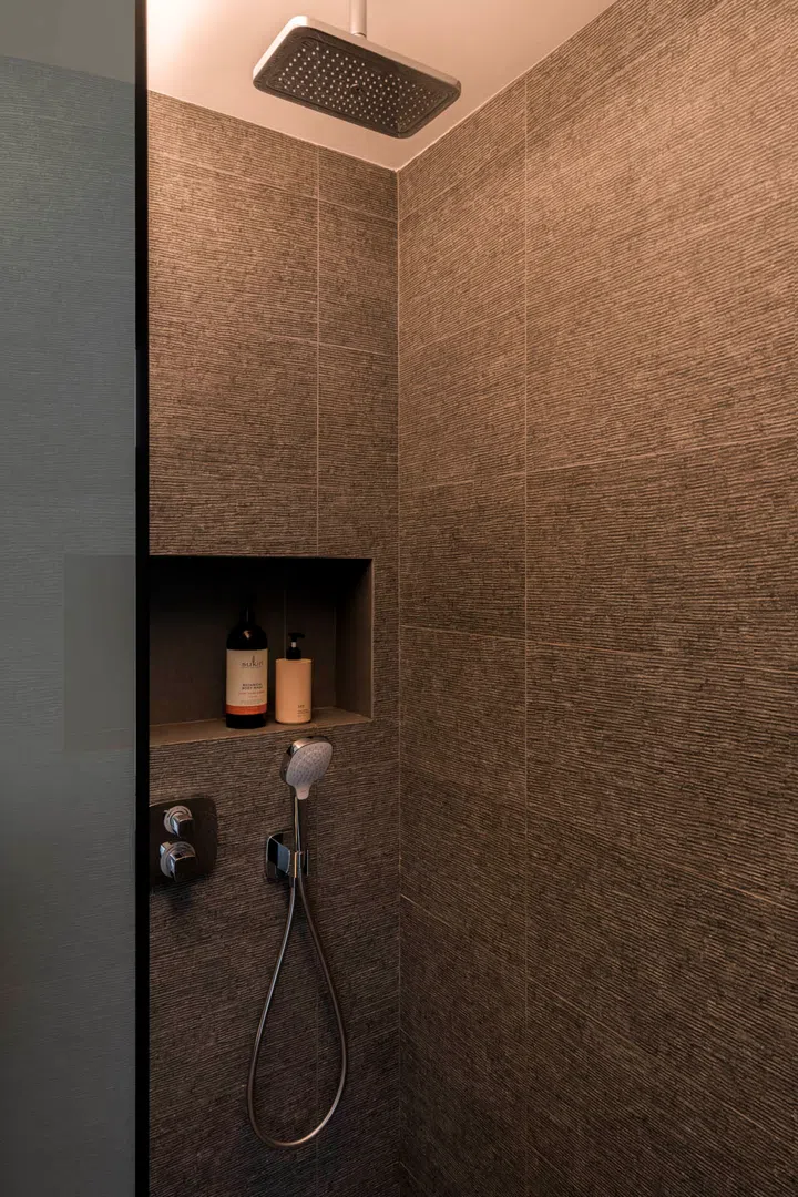 The master bath conceals piping behind a tiled false wall, which doubles as a built-in niche.