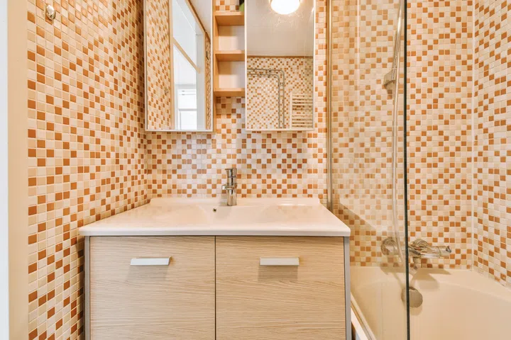 Bathtub with glass shower placed in corner near sink and mirror in small light bathroom with white tile walls