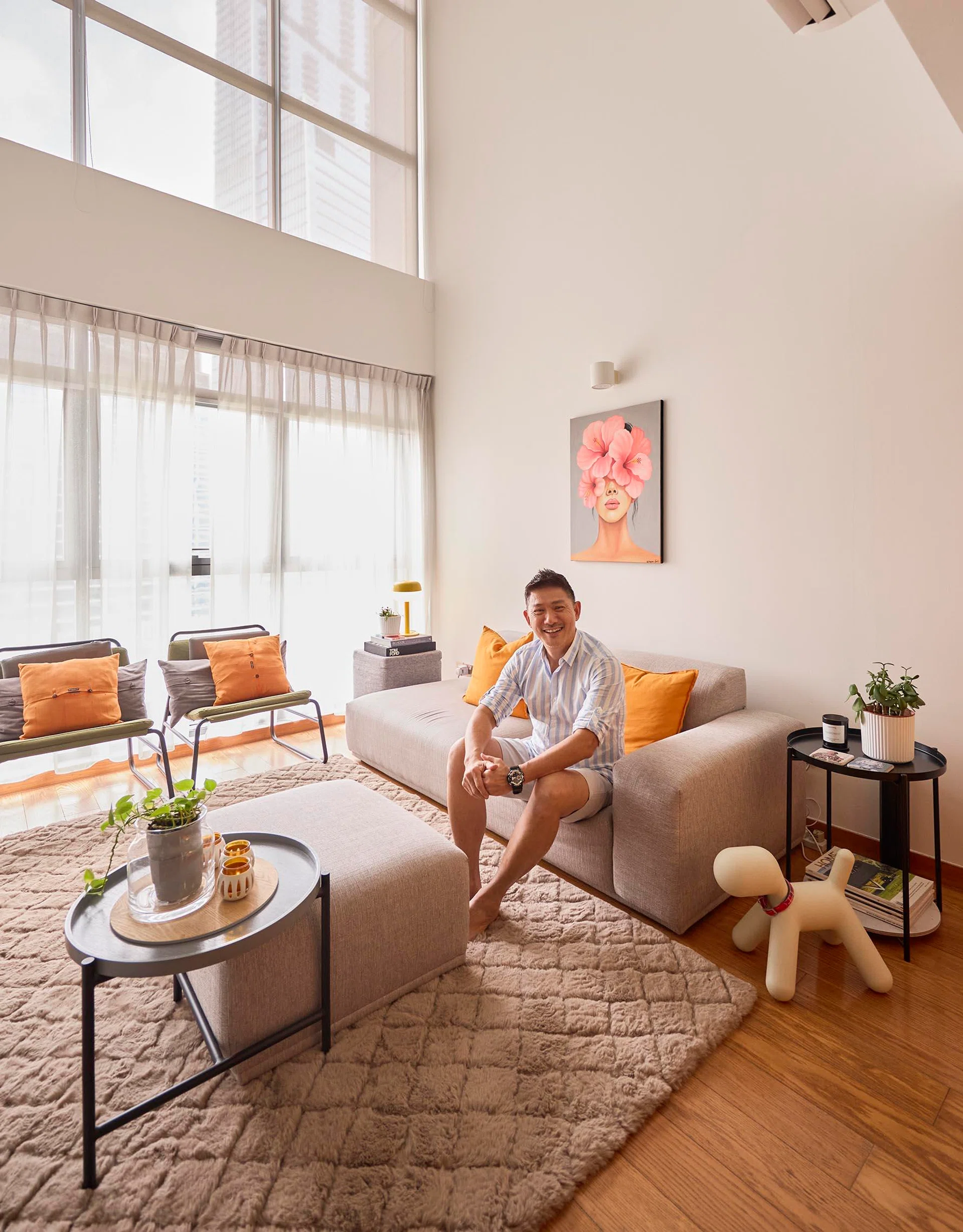 Terence in the double-volume living room, where tall windows flood the loft with daylight and warm orange accents reflect his signature colour palette.