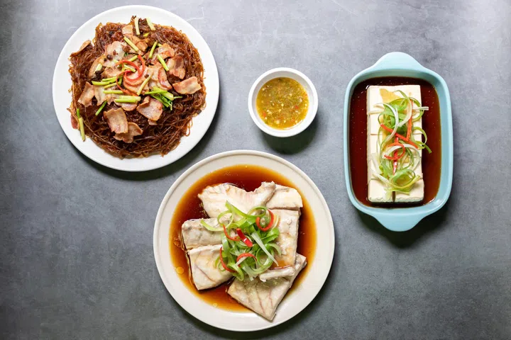 Sea bass fillet steam with soy sauce, shrimp potted with vermicelli and vegan silken tofu is served hot or cold with a savory soy sauce. Top view on black table background.