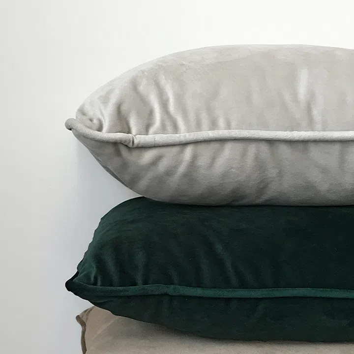 A stack of brown, black, and grey pillows against a white wall.