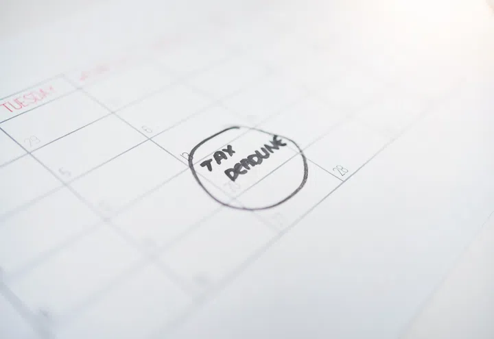 Writing, calendar and tax deadline on schedule planner for date, commitment or reminder on paper. Text, finance or budget plan for time, day or message note in financial deduction or monthly planning.