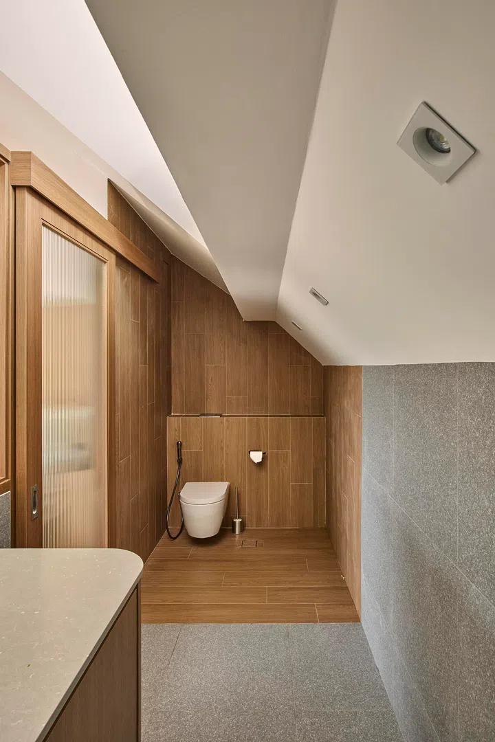 The WC is defined by wood-look finishing, creating a warmer contrast against the cooler stone surfaces elsewhere.