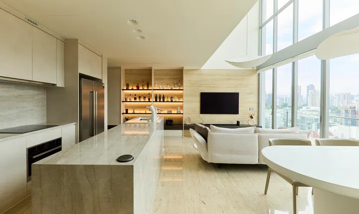 The open-plan layout reveals a clear visual connection between the travertine kitchen counter and the soaring floor-to-ceiling windows, inviting natural light deep into the living space.