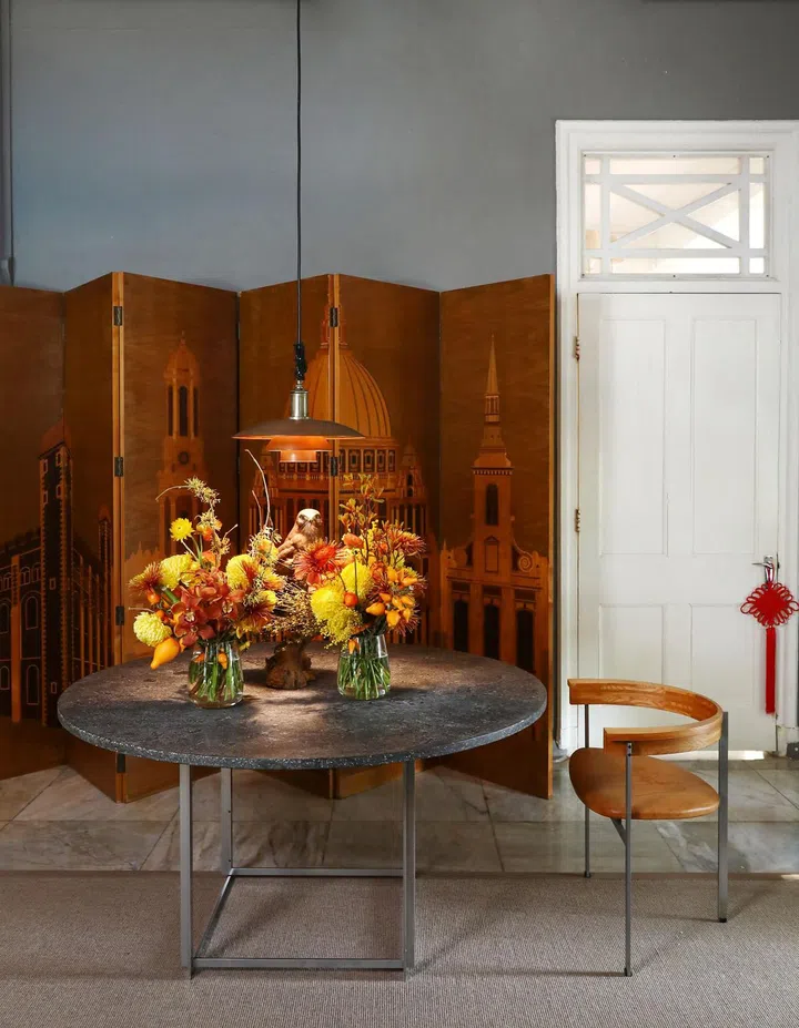 A specially commissioned veneer screen of the London skyline from Linley provides a backdrop to a couple of Chinese New Year flower decoration blooms in 1B2G Fine Vintage Furniture store owner, Lynette Wong's house.