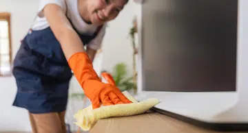 A cheerful woman dons bright orange gloves as she diligently wipes down the surface.