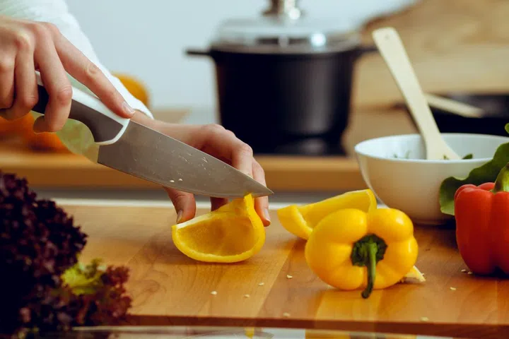 Closeup of human hands cooking vegetables in kitchen. Housewife slicing bell pepper.