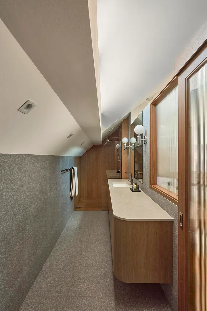 A long vanity runs the length of the bathroom, with material changes subtly dividing the space into zones.