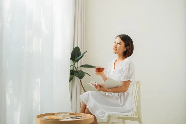 young-pretty-woman-sitting-near-window-drinking-tea-reading-book-enjoys-rest