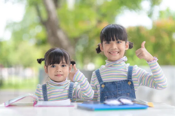 Two student little Asian girls reading the book on table.