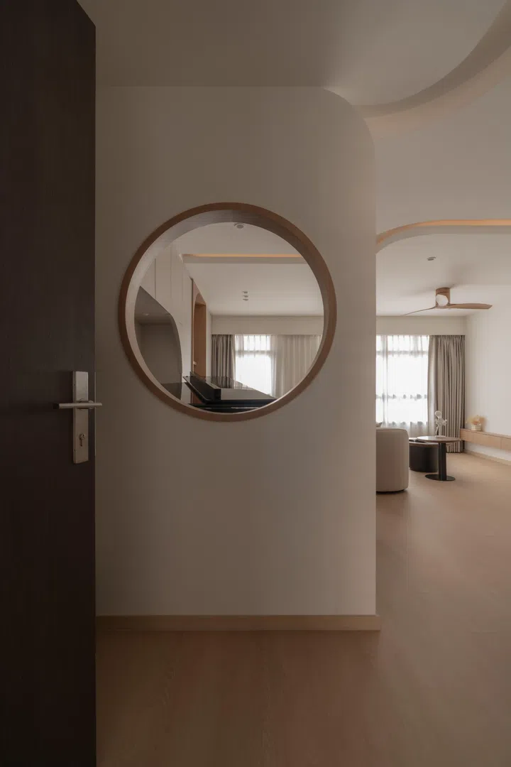A curved foyer wall with a circular opening offers a soft transition into the home, framing views through to the living area while quietly introducing the design’s flowing language.