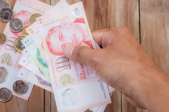 Hand holding Singapore money on wooden table background, various of singapore dollar banknote