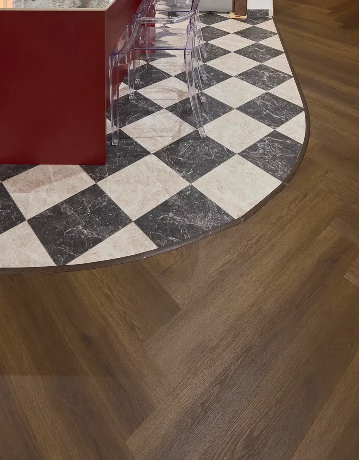 The junction between herringbone vinyl and checkerboard tiles is executed in a soft curve, requiring close coordination between trades.