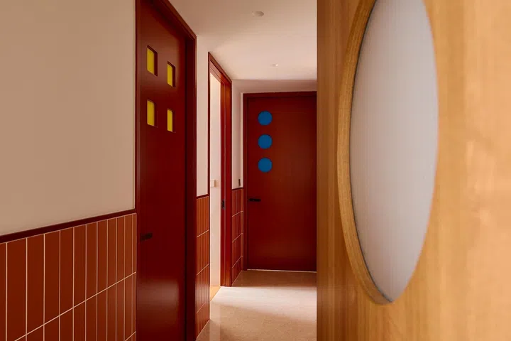 Each bedroom door features a different arrangement of coloured windows, adding a playful touch to the warm timber-and-terracotta corridor.