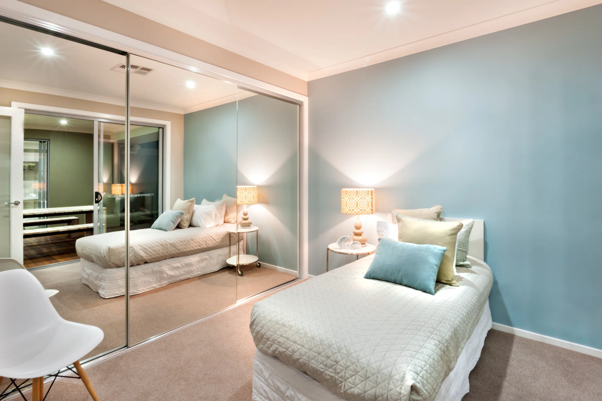 Modern and classic bedroom walls are light blue, which is illuminated in lights of the table lamp and one wall is totally covered with big mirrors.