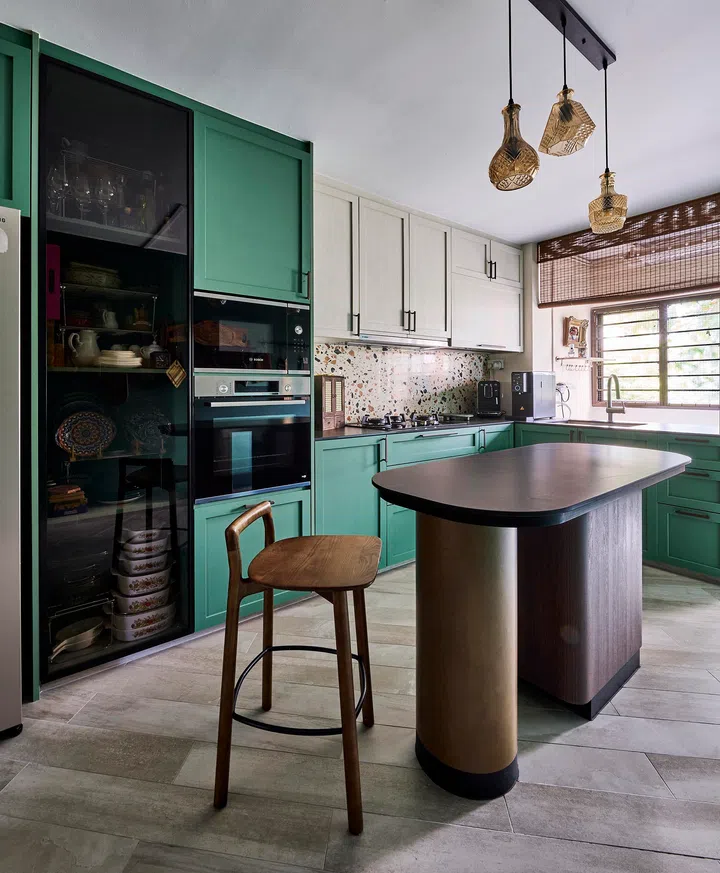 The compact green kitchen, brightened by woven pendant lamps and terrazzo accents, opens into a warm and functional space in a 4-room HDB resale in Sunset Way.