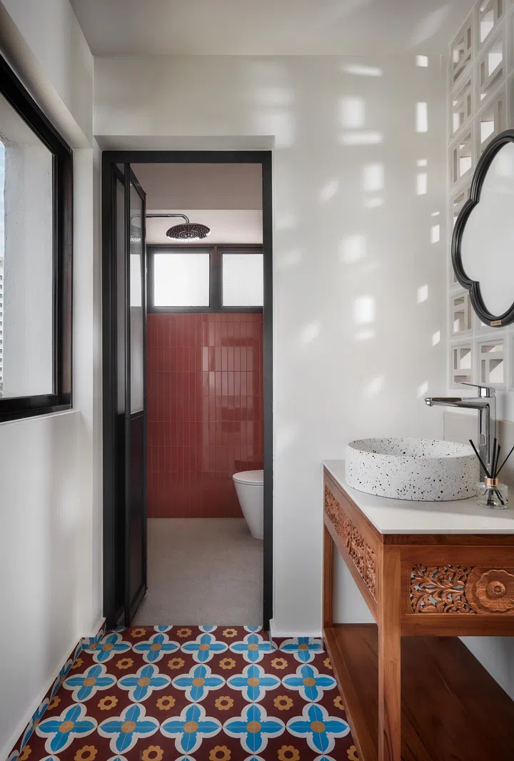 A hand-carved teak basin stand sits outside the common bathroom, while glossy terracotta tiles inside continue the home’s warm, grounded palette.