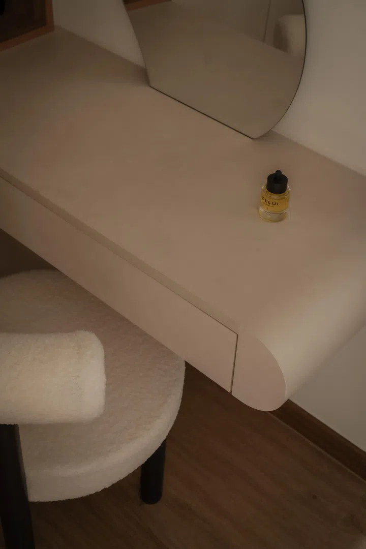 A curved vanity counter with softened edges and a sculptural stool continues the home’s gentle design language within the walk-in wardrobe.