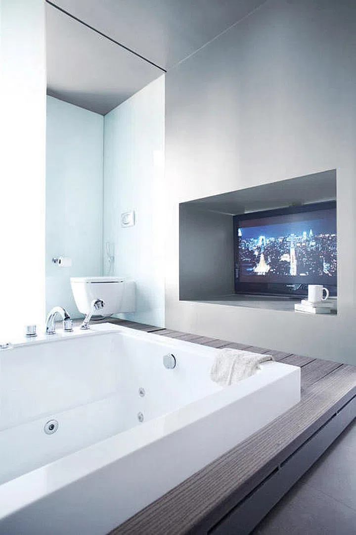 Recessed TV console in a bathroom set before a bathtub.