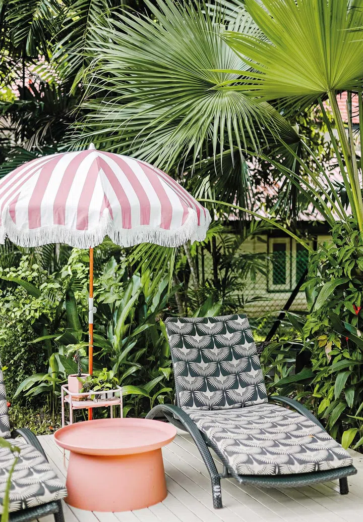 A patterned deck chair with a pink and white striped beach umbrella