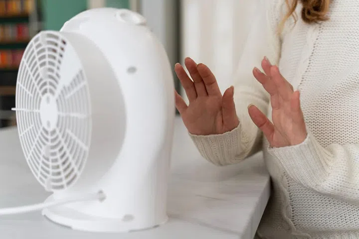 woman-warming-up-hands-near-heater