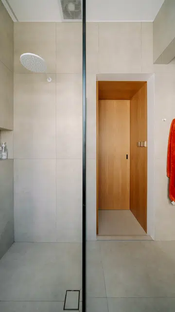 Floating oak cabinetry, large-format tiles and a frameless glass shower enclosure continue the home’s warm, understated material palette into the bathroom.