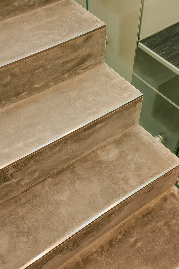 Concrete-look treads and glass balustrades balance weight and lightness, helping the stair read as an important spatial marker rather than just a connector.