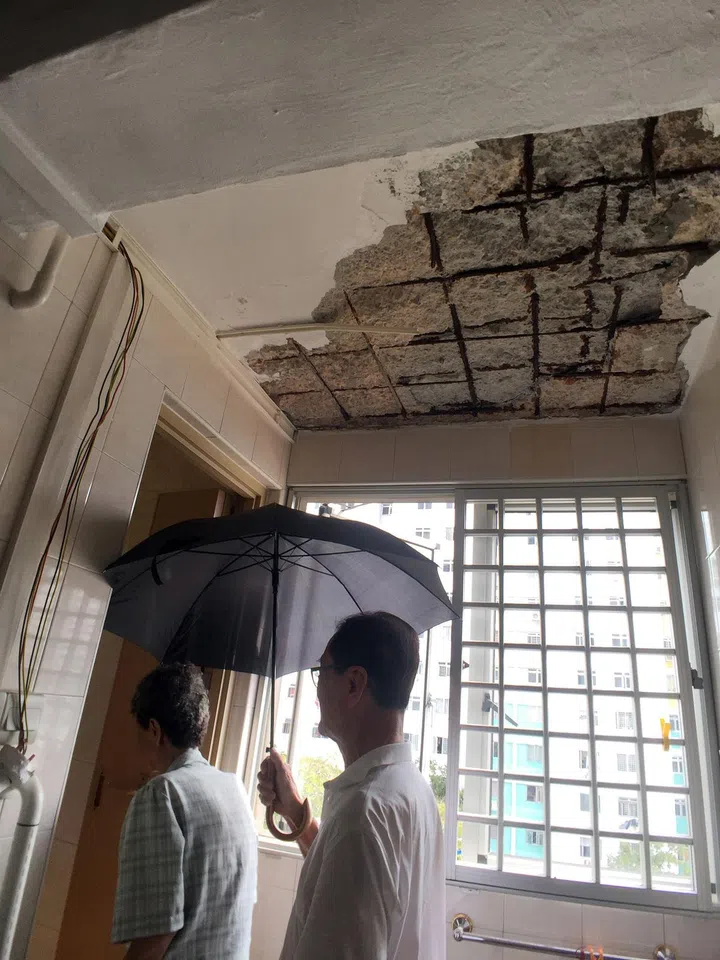 Mr Lee shielding Madam Chen with an umbrella on her way to the toilet near the kitchen, where pieces from the ceiling fell on Monday. HDB officers later visited the Marine Terrace flat and temporary repair work was done to prevent a recurrence.