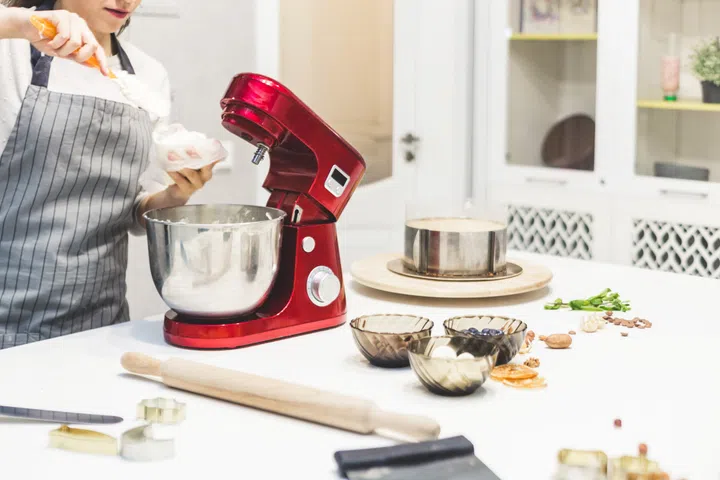 Young female confectioner whips cream in a metal bowl in a red electric mixer. The concept of homemade pastry, cooking