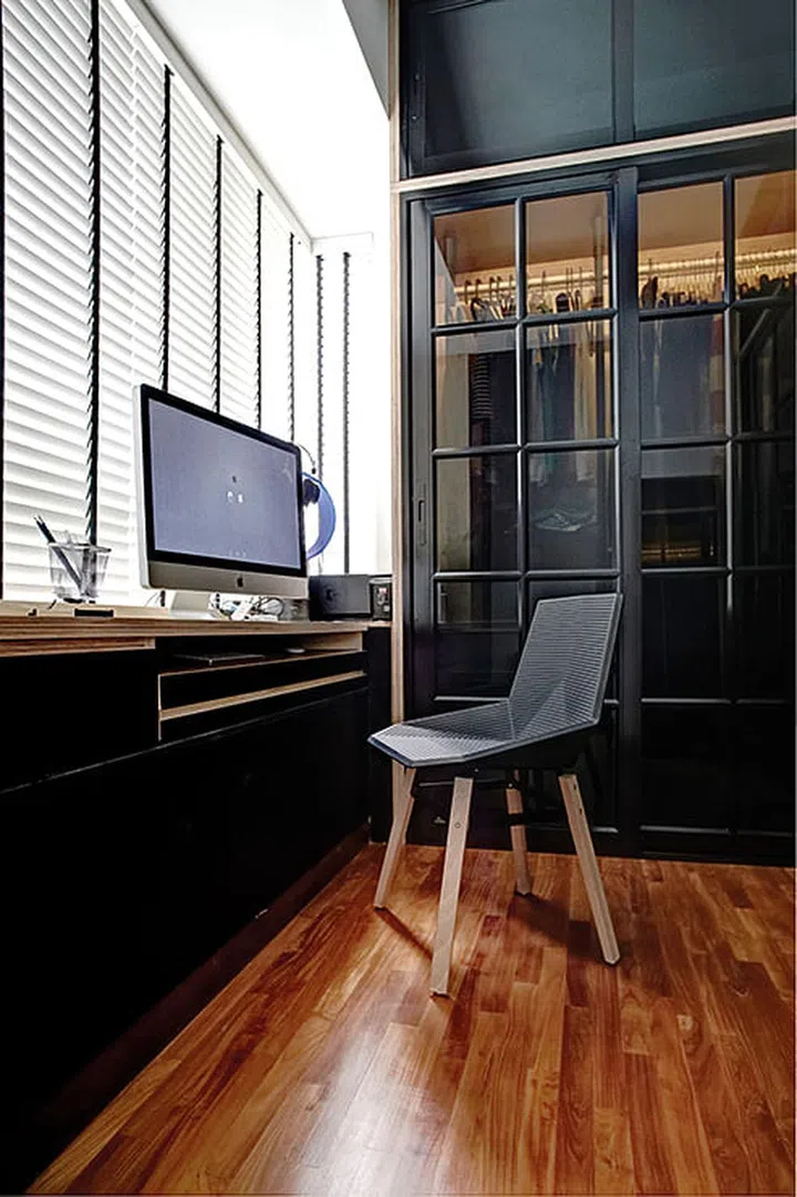 The home office houses a spacious but discreet wardrobe hidden behind tinted black sliding glass panels, which are a contemporary take on the industrial look. Interior design by JQ Ong/ The Association.