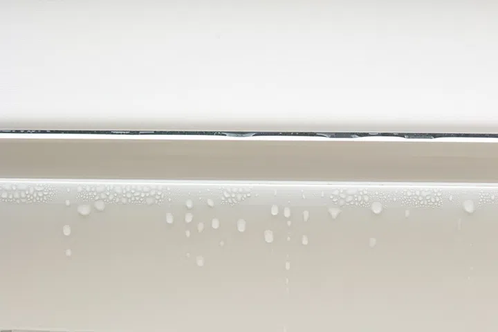 Water droplets condensation on white metal-plastic frame of window indoors room. High humidity. Moisture condensation problems, hot water vapor condensed on window in cold season.