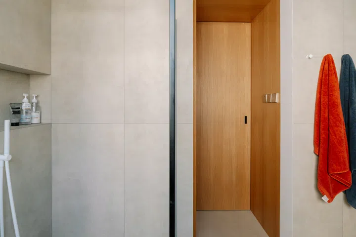 Floating oak cabinetry, large-format tiles and a frameless glass shower enclosure continue the home’s warm, understated material palette into the bathroom.