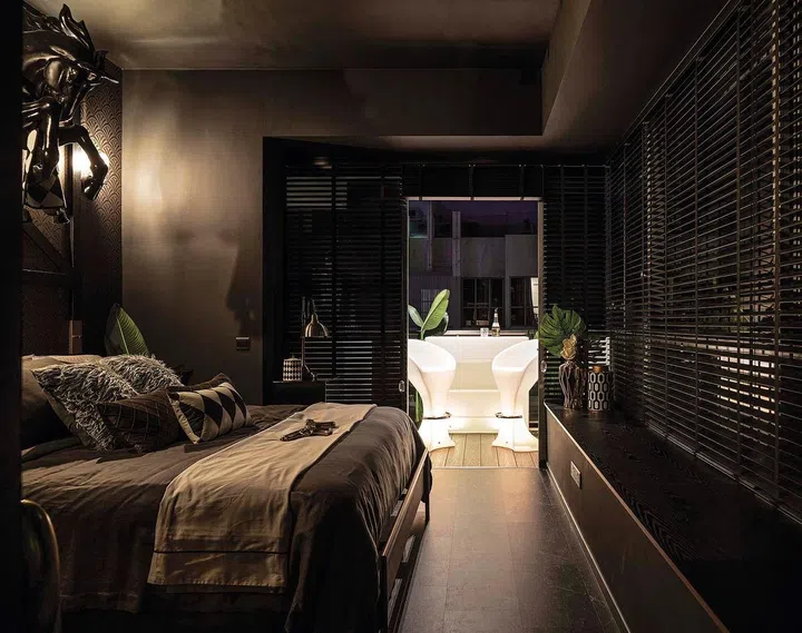 The master bedroom features black marble-textured vinyul flooring with white veins. LED-lit outdoor furniture light up the balcony area beyond, evoking the perfect chill-out vibes. 