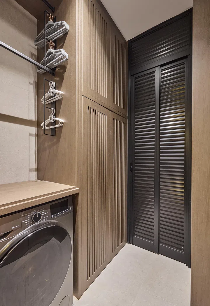 A well-organised space featuring ample storage cabinets and hanging rails, with the washing machine tucked neatly away.