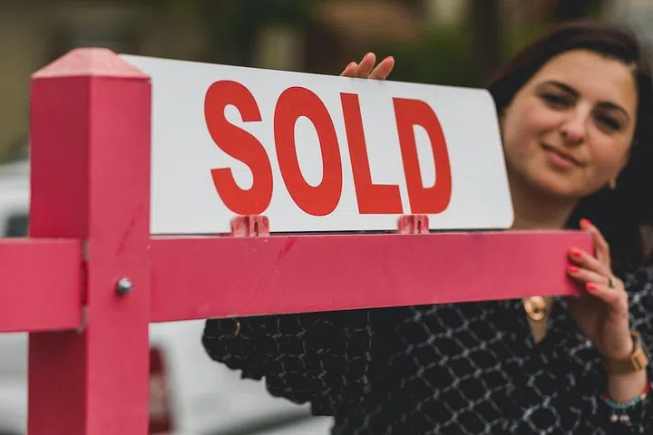 A woman displaying a "Sold" standing signage.