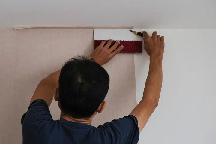 Man install cut wallpaper on white wall.