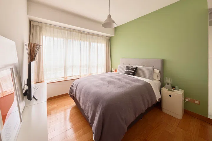 The bedroom is kept simple and calm, with a soft green wall and filtered daylight shaping a quiet, restful atmosphere.