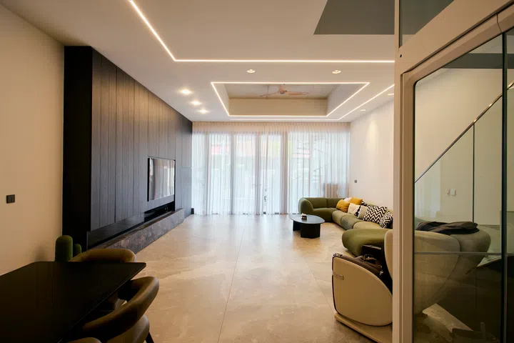 At the front, the living area is kept minimal and uncluttered, allowing natural light filtered through full-height curtains to soften the space throughout the day.
