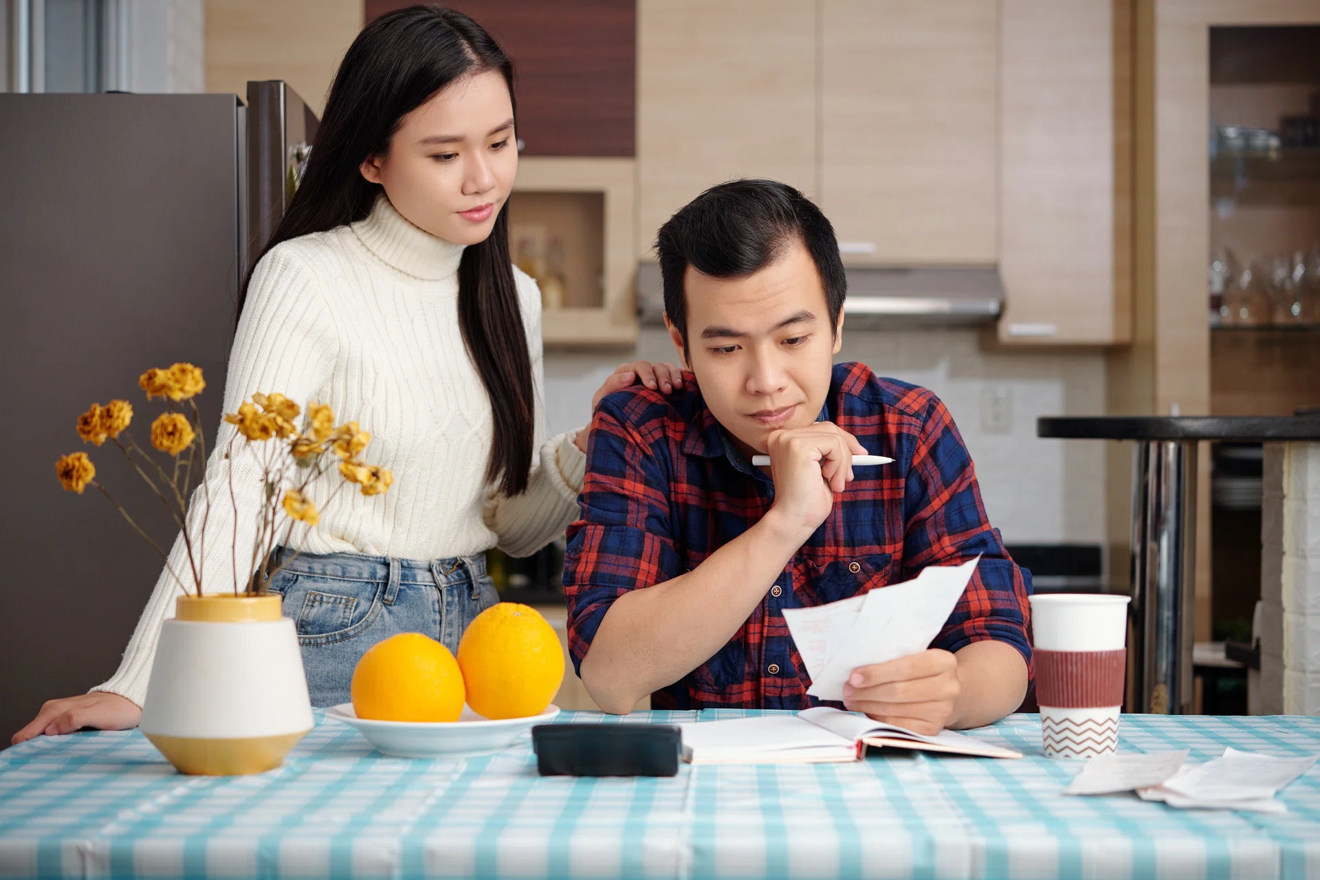 Young asian couple sitting at table in the kitchen and calculating bills.