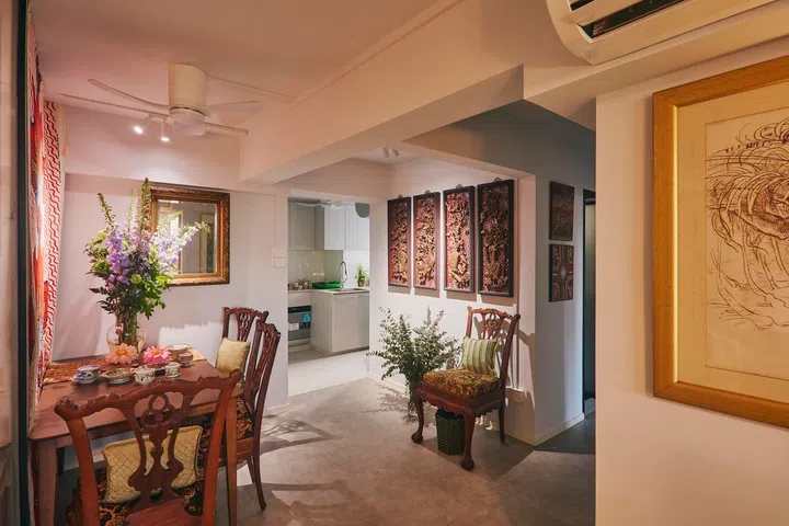 The dining area connects the living room and kitchen, with carved timber artworks and fresh flowers creating layers of visual interest throughout the space.