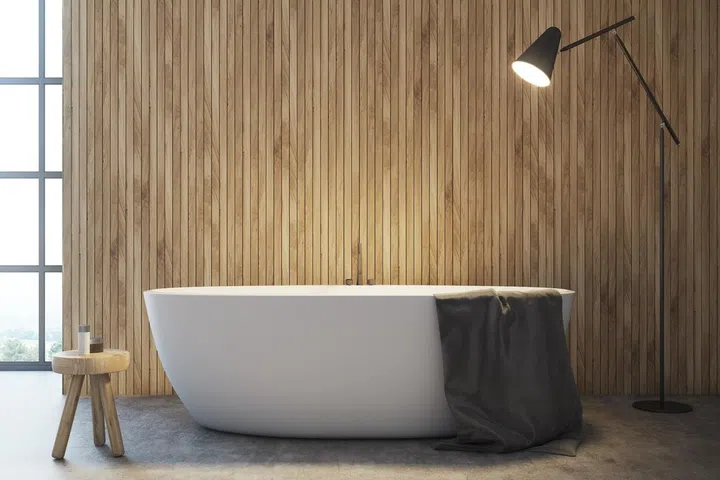 Interior of modern bathroom with wooden walls, concrete floor, comfortable white bathtub and gray towel on it.