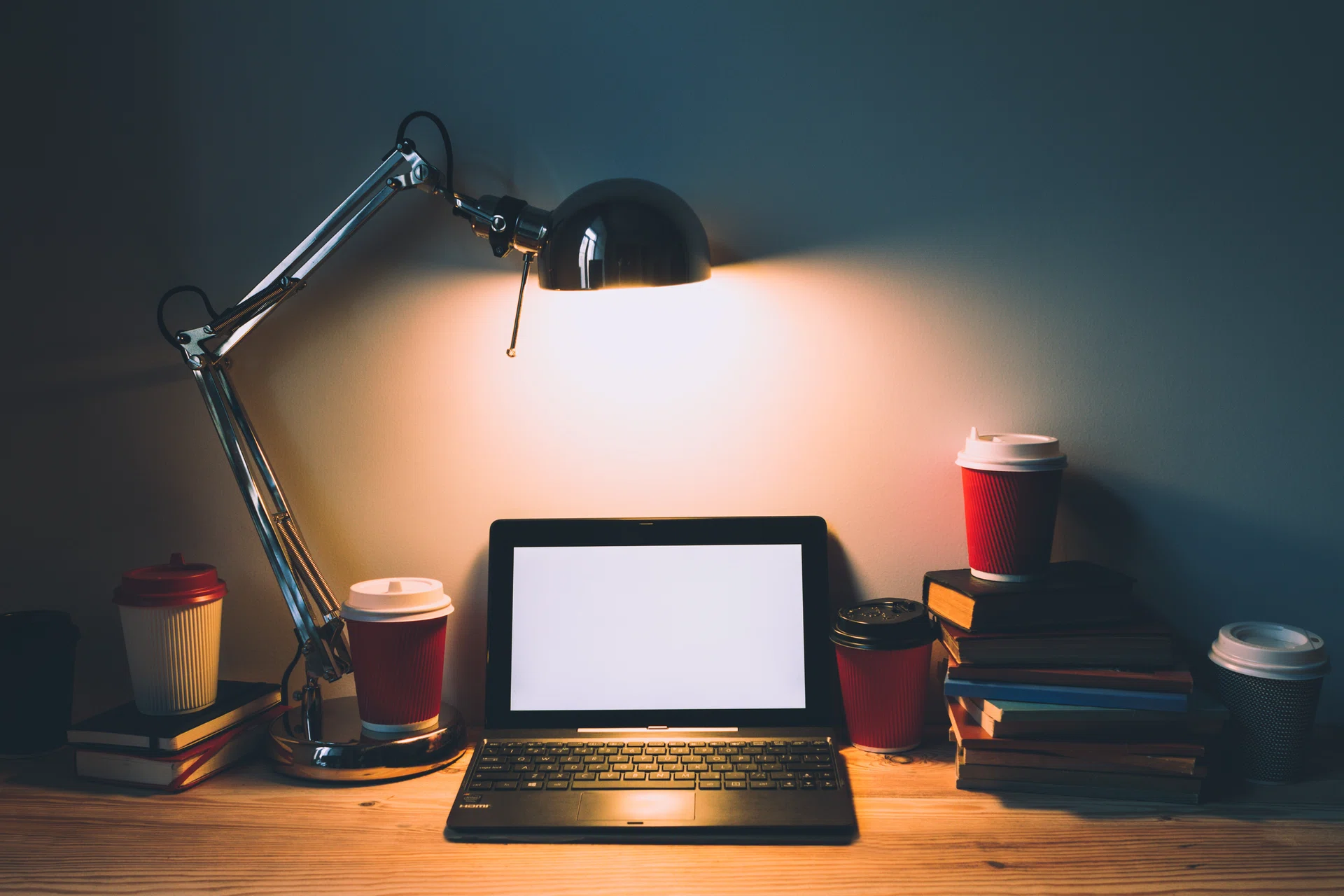 Netbook, books, coffee in paper cups on the table under the light lamp