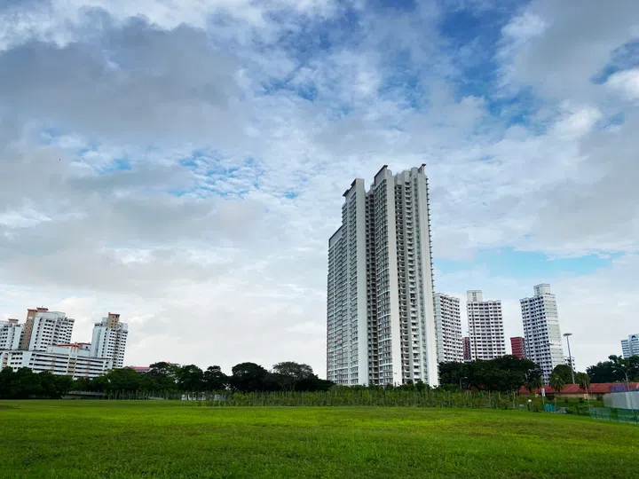 Distant view of residential apartment (HDB) with empty field under cloudy sky.