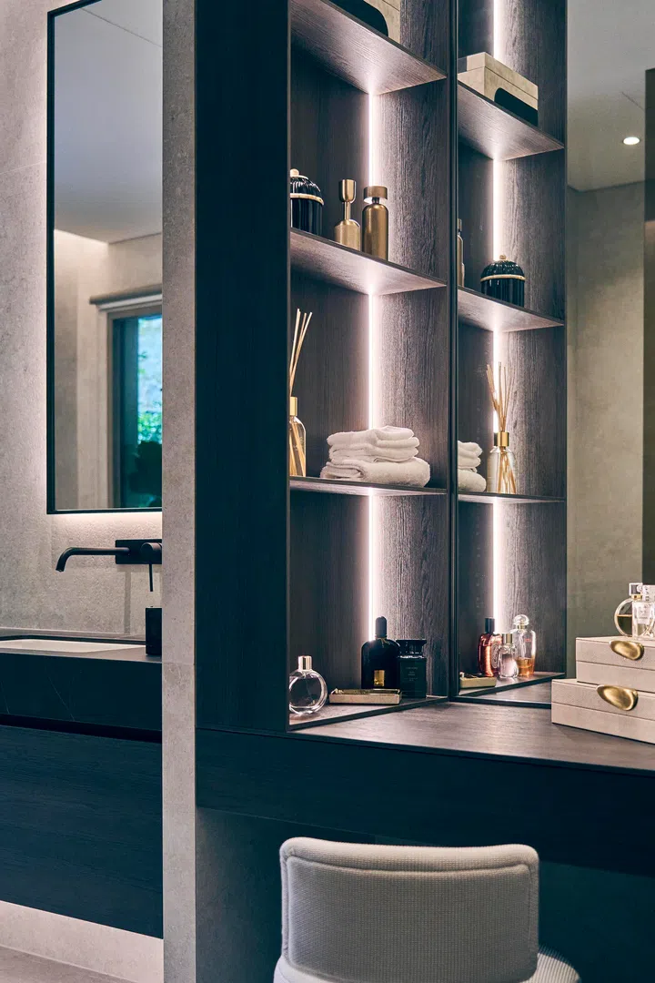  A dedicated makeup and dressing area extends the bathroom’s function, with illuminated shelving for display and storage.
