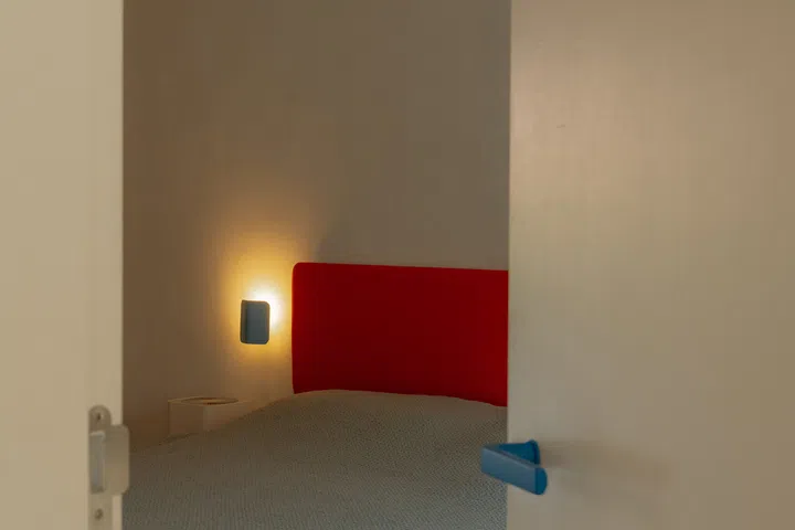 The master bedroom continues the home’s restrained palette, with a bold red upholstered headboard providing a subtle burst of colour.