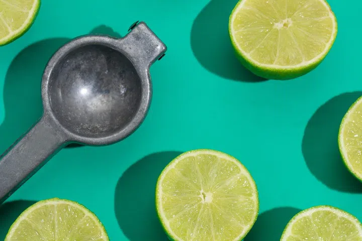 Cutted lime and metallic squeezer on green background