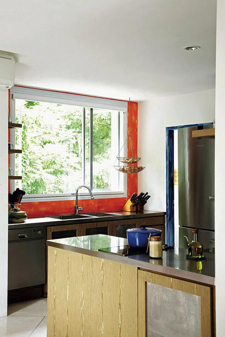 The fresh green view is framed by the hand-painted kitchen feature wall. The blue door frame completes the contrast.